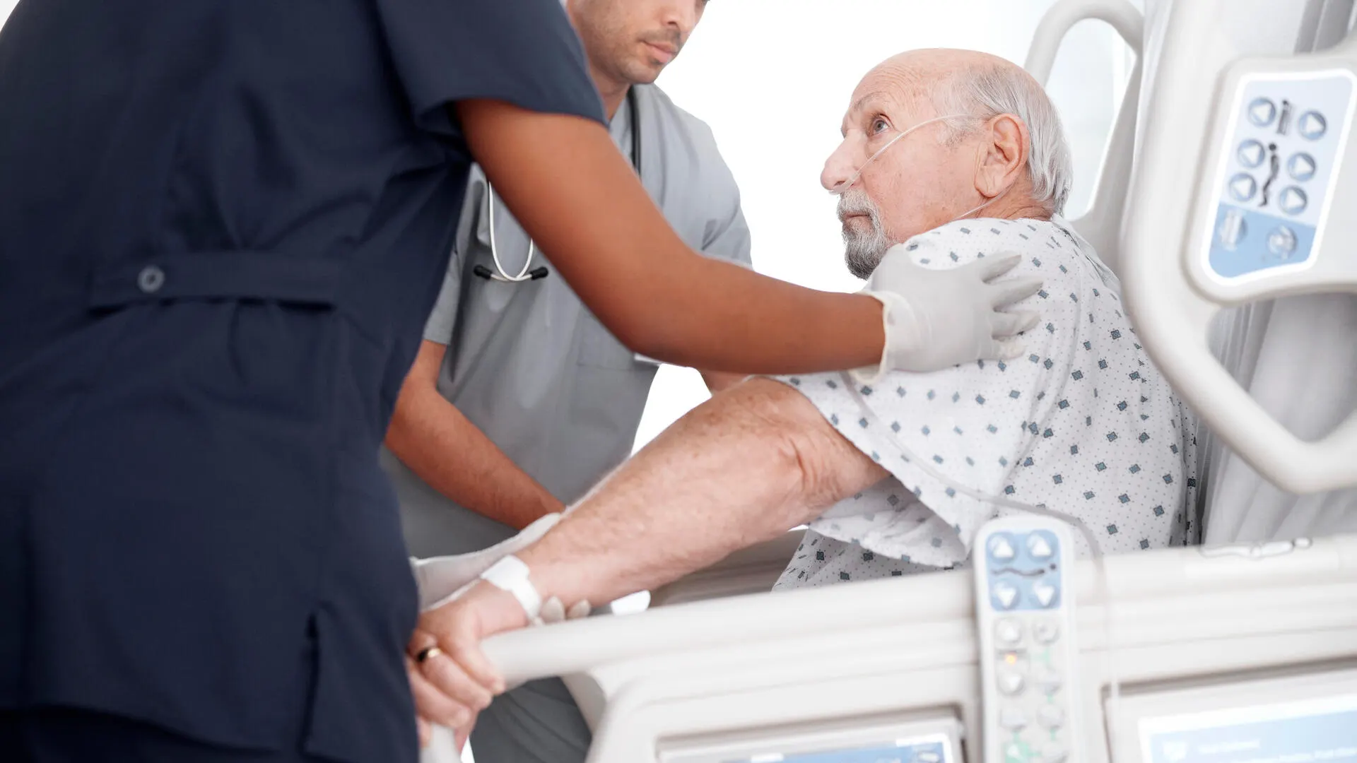 Caregivers helping a patient stand using Baxter Progressa plus bed